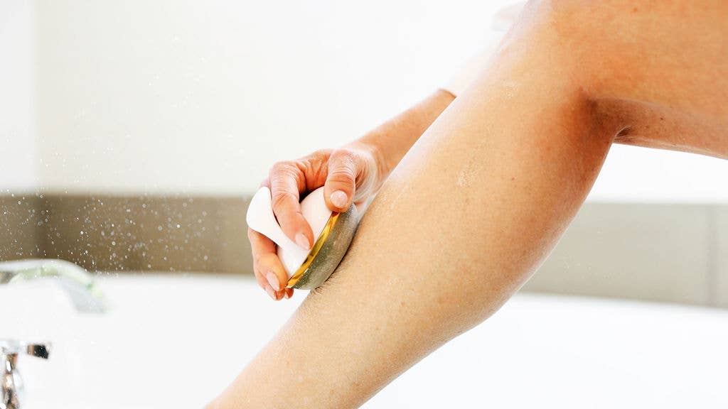 Closeup image of Firmaglow microderm device being used to smooth the skin on the leg of a model who is sitting on the edge of a bathtub. 