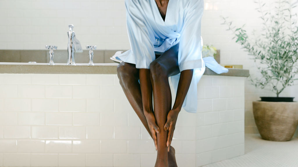 woman sitting on the bathtube in a blue robe with smooth legs